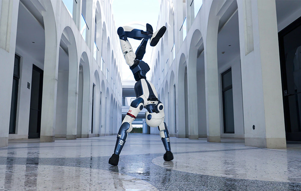 Un robot umanoid alb și albastru care execută o stândă pe mâini precisă într-un coridor modern alb, cu arcade