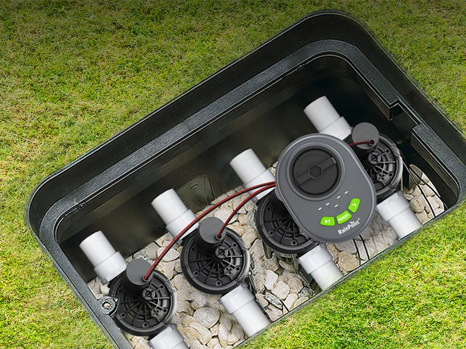 Controler RainPoint instalat într-o cutie cu patru supape pe un fundal de gazon.