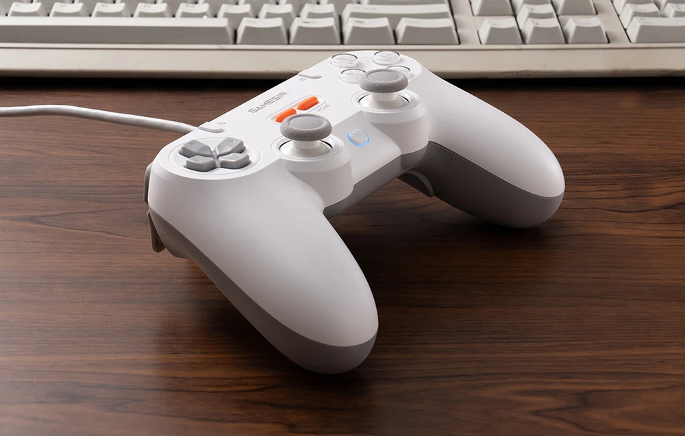 Un controller GameSir alb așezat pe o masă în fața unei tastaturi clasice de computer.