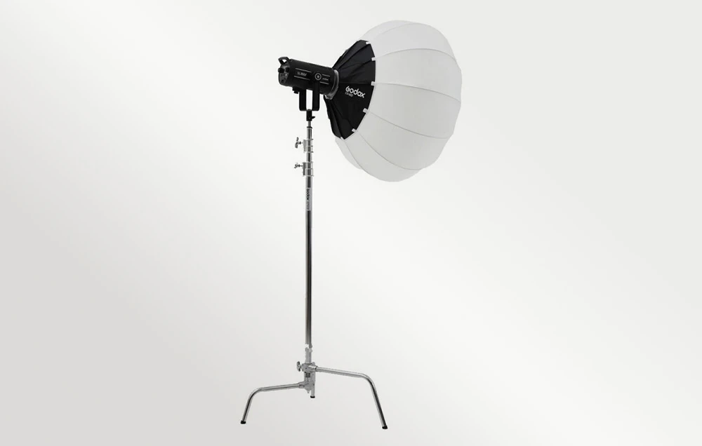 O softbox rotundă albă pe o lampă de studio neagră, montată pe un stativ de iluminat argintiu înalt, pe un fundal deschis.