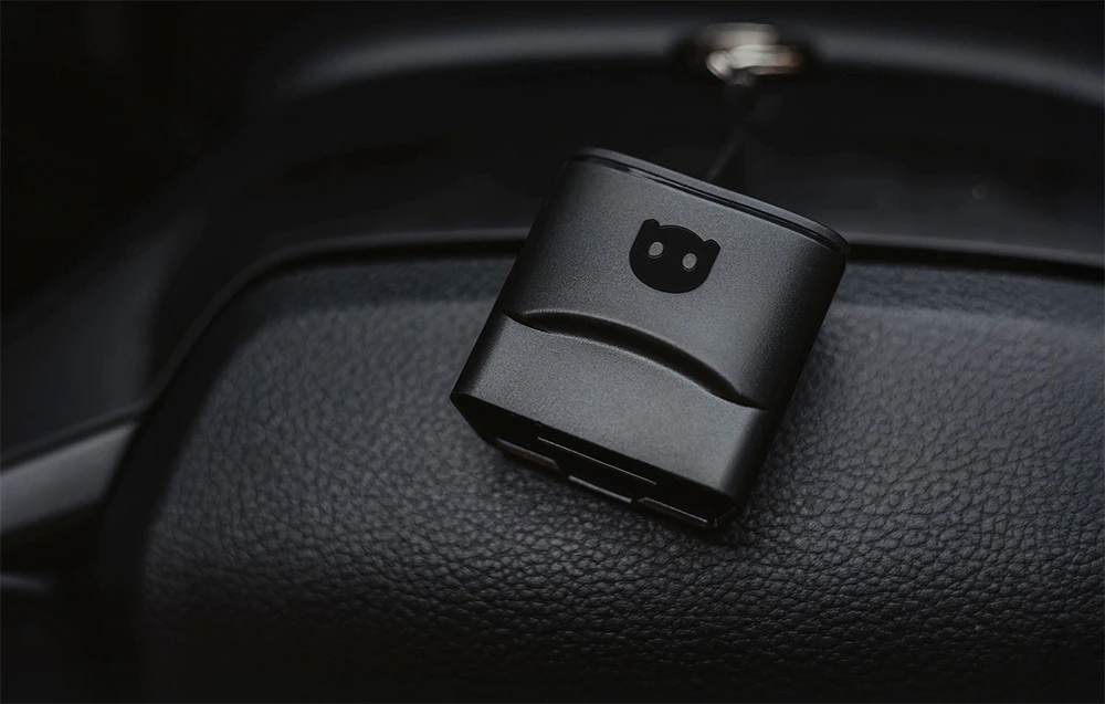 Adaptor de diagnosticare Carly OBD2 negru așezat pe bordul din piele al mașinii