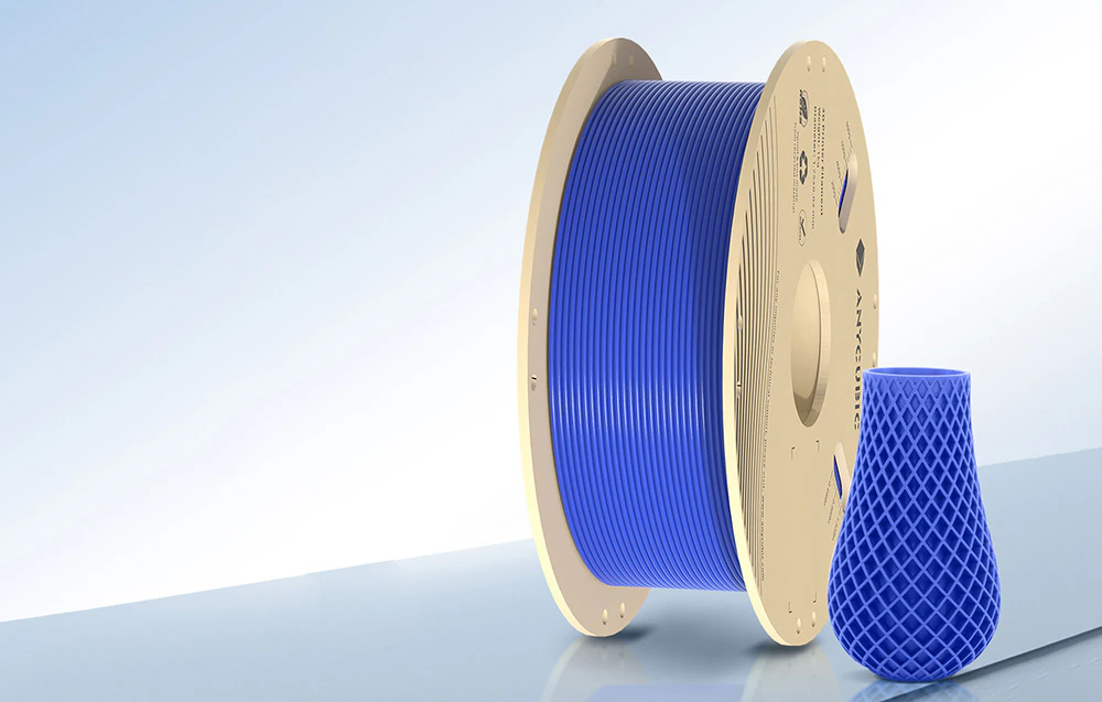 Filament albastru lângă un model 3D pe o masă de lucru albastră.