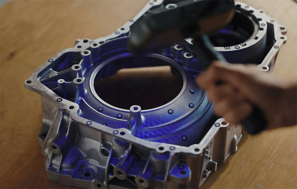Un scaner 3D portabil scanează o carcasă mecanică metalică așezată pe o masă