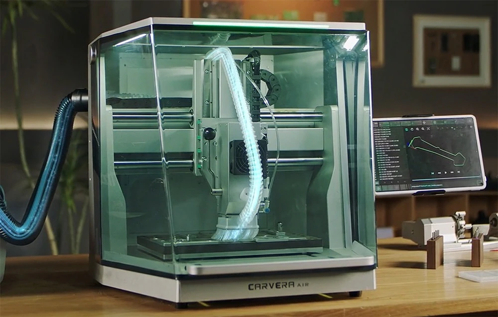 Routerul CNC MAKERA Carvera Air se află pe o masă în atelier, lângă modelele finite