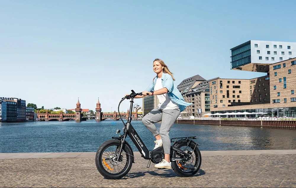 O femeie merge pe o bicicletă electrică neagră de-a lungul malului într-un oraș modern