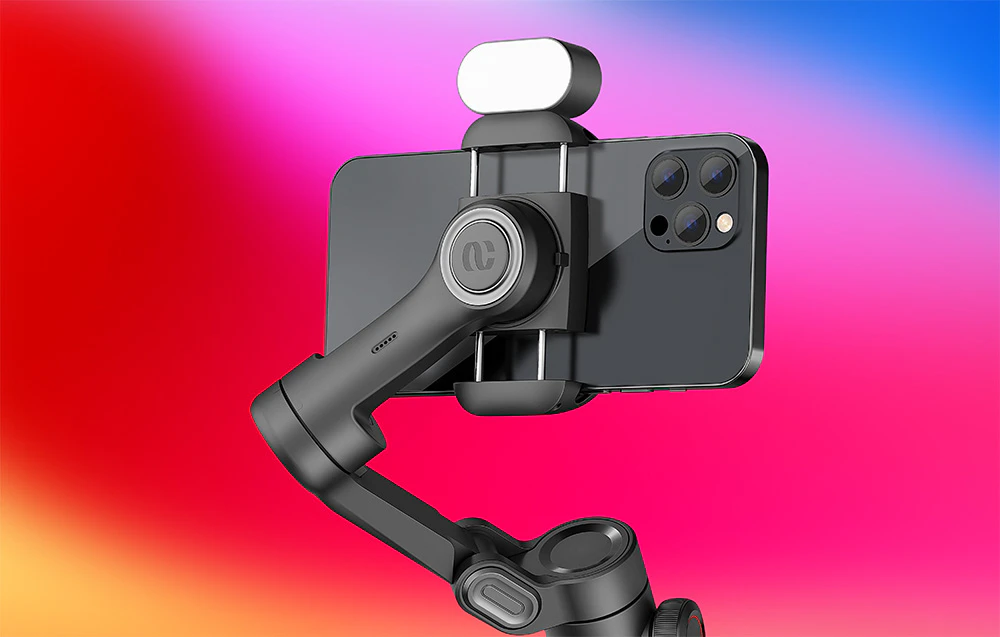 Prim-plan al unui smartphone montat într-un suport pentru gimbal cu un modul suplimentar în partea superioară, pe un fundal colorat.