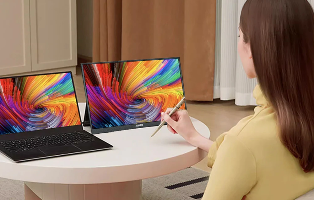 O femeie care desenează cu un stylus special pe ecranul tactil al unui monitor așezat lângă un laptop.