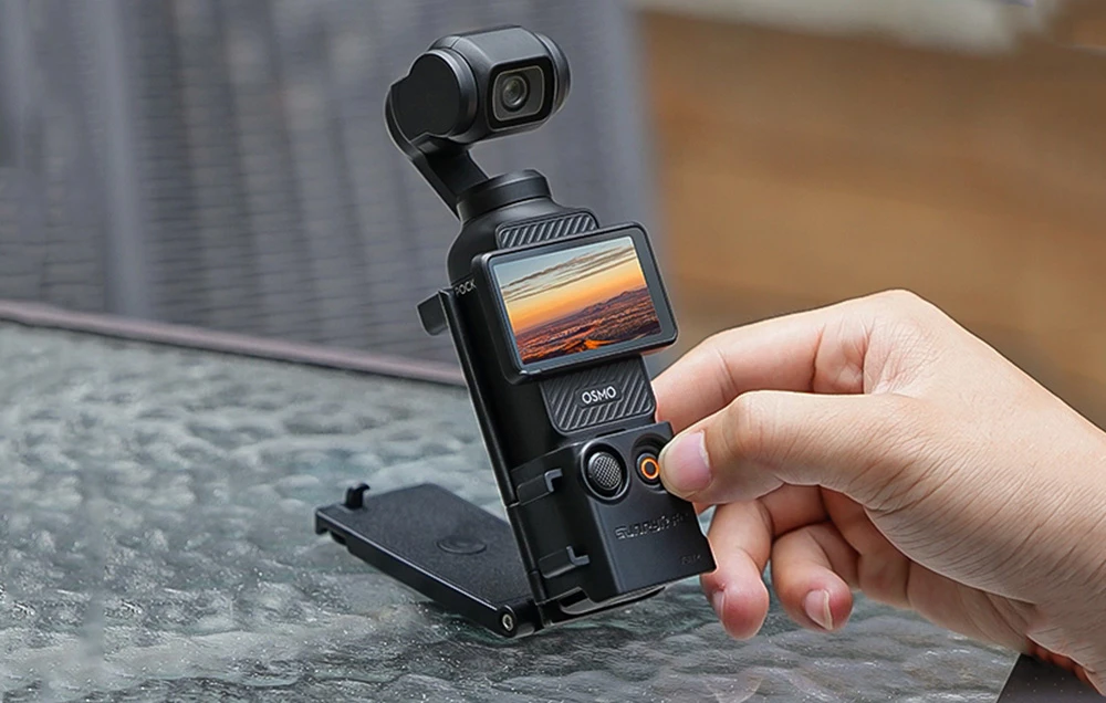 Camera DJI Pocket pliată pe o masă, cu suportul întins și mâna întinsă spre buton