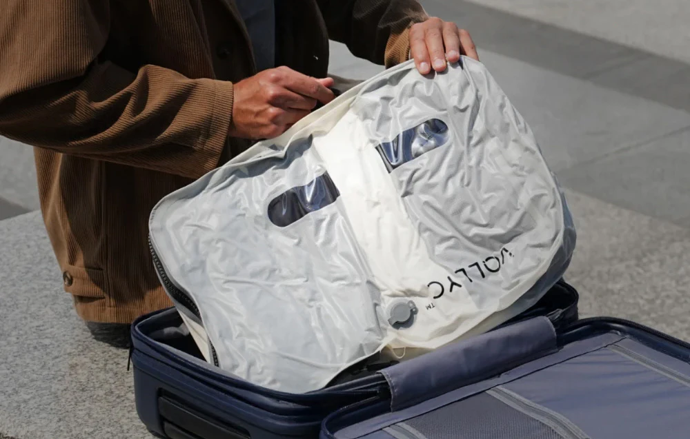 Mâini care țin un sac transparent de vid cu supapă deasupra unei valize deschise