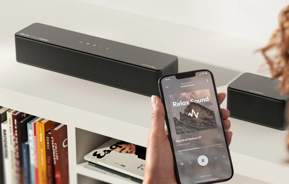 Difuzoare Ultimea și subwoofer amplasate în sufragerie lângă o canapea albă lungă