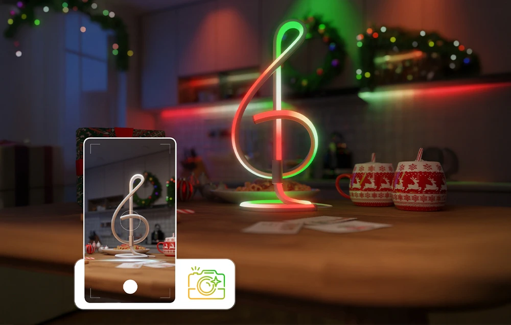 Ecranul unui smartphone orientat spre o lampă de birou roșie și verde așezată pe o masă cu căni de sărbători.