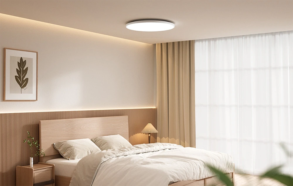 Dormitor luminos cu pat și plafonieră inteligentă Yeelight Mercury C300 aprinsă.