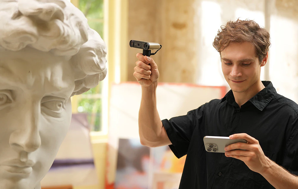 Un bărbat îmbrăcat într-o cămașă neagră folosește un scaner 3D pentru a digitaliza o sculptură a unui cap într-un studio