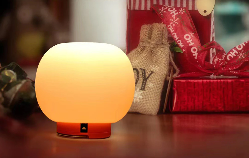 O lampă de călătorie cu lumină caldă pe masa de lângă cadouri și decorațiuni de Crăciun