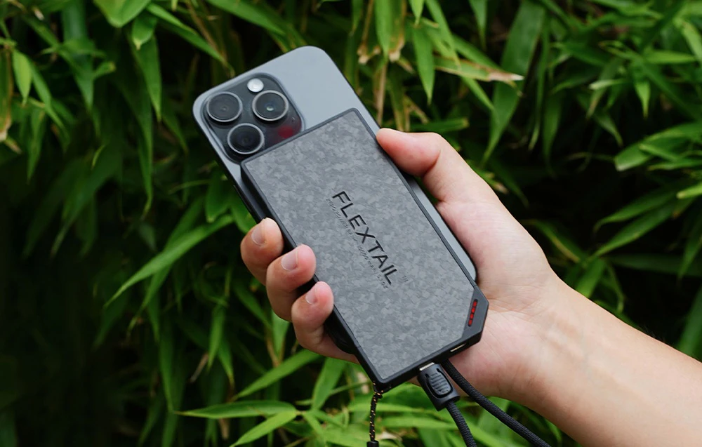 Un smartphone conectat prin cablu la o baterie externă FLEXTAIL ținută în mână.