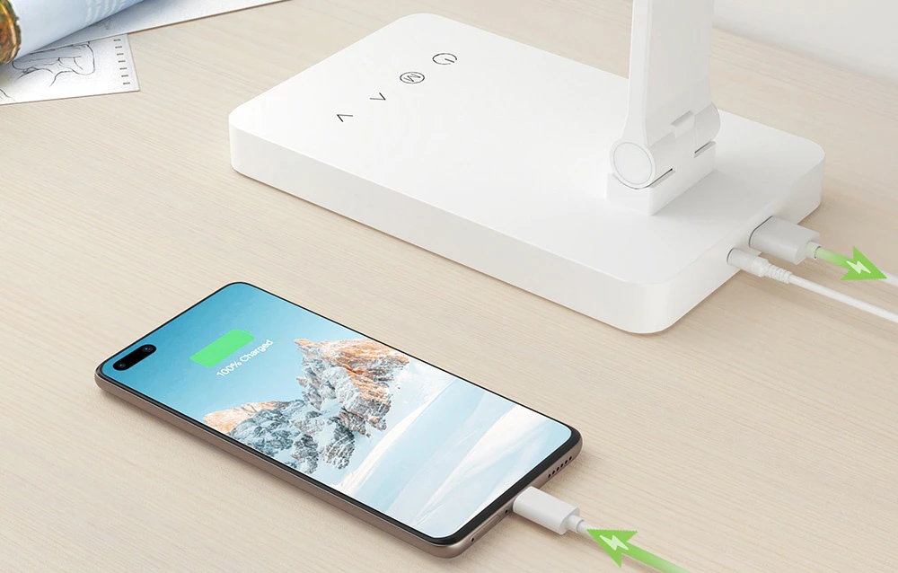 Un prim-plan al bazei lămpii cu un cablu USB conectat, care încarcă un smartphone așezat pe masă