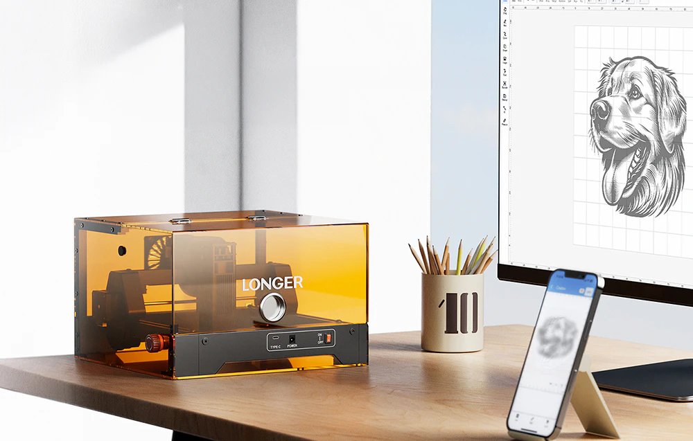 Gravor laser într-o carcasă portocalie conectat la un computer cu un desen cu un câine vizibil pe monitor și smartphone