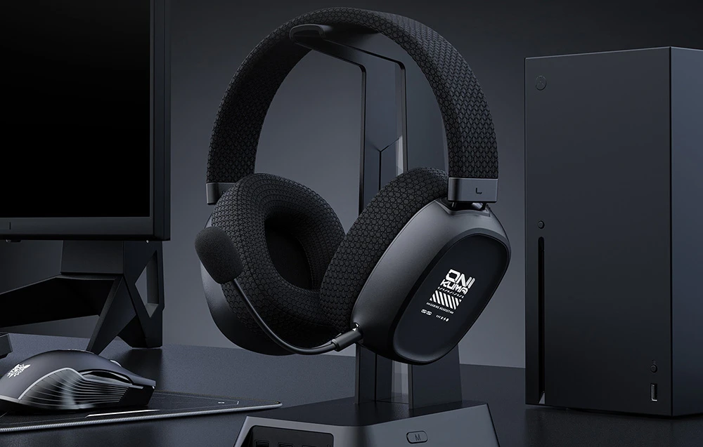 Căști de gaming negre pe suport lângă consolă și monitor pe birou