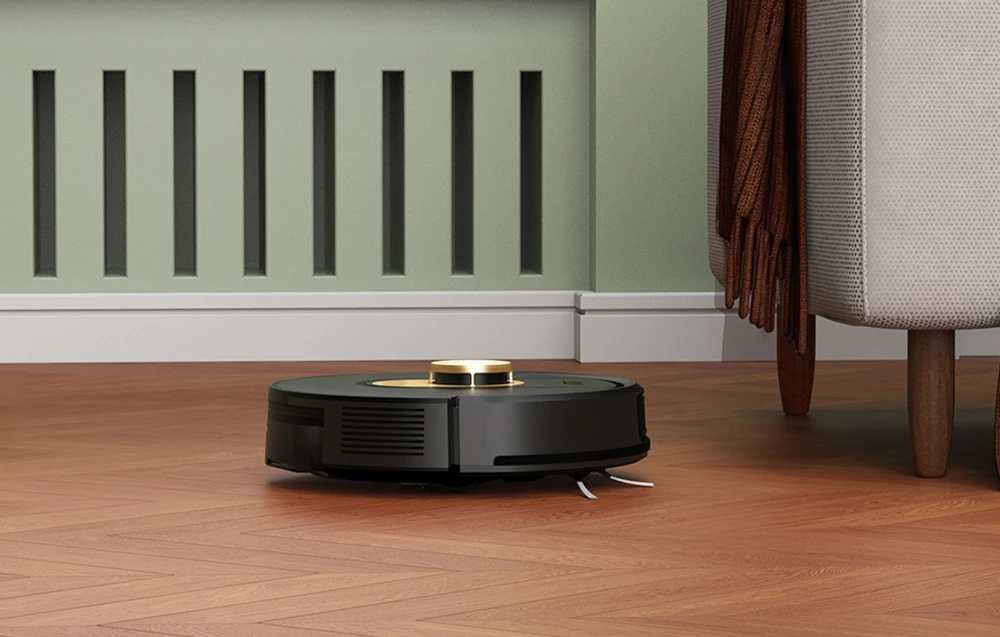 Un robot de curățenie negru cu un senzor auriu, așezat pe podeaua din parchet lângă un fotoliu
