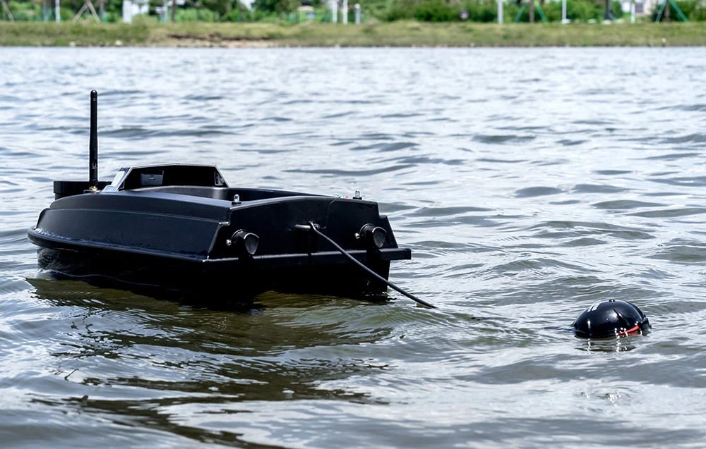 O barcă de momeală neagră cu o antenă și un senzor sonar atașat la o linie, plutind pe un lac
