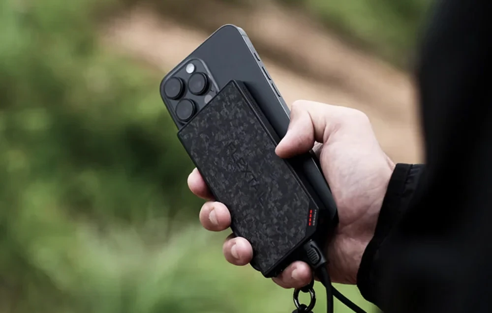 O mână ține un smartphone conectat prin cablu la bateria externă FLEXTAIL.