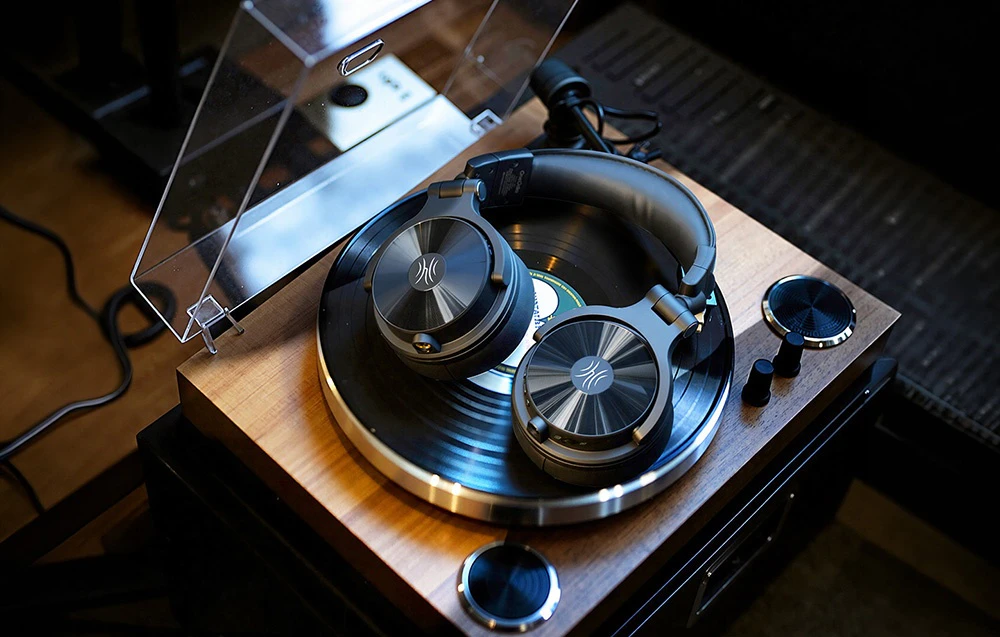 Căști wireless negre așezate pe un platan cu un disc de vinil sub un capac transparent