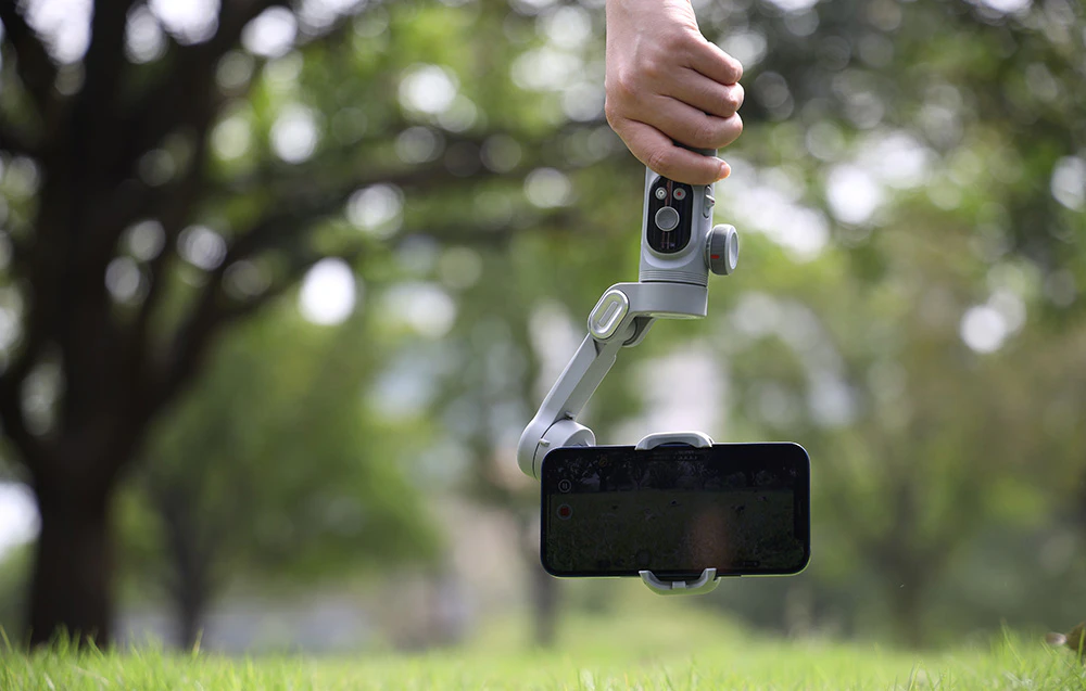 Un gimbal cu un smartphone ținut deasupra ierbii în timp ce se filmează în aer liber.