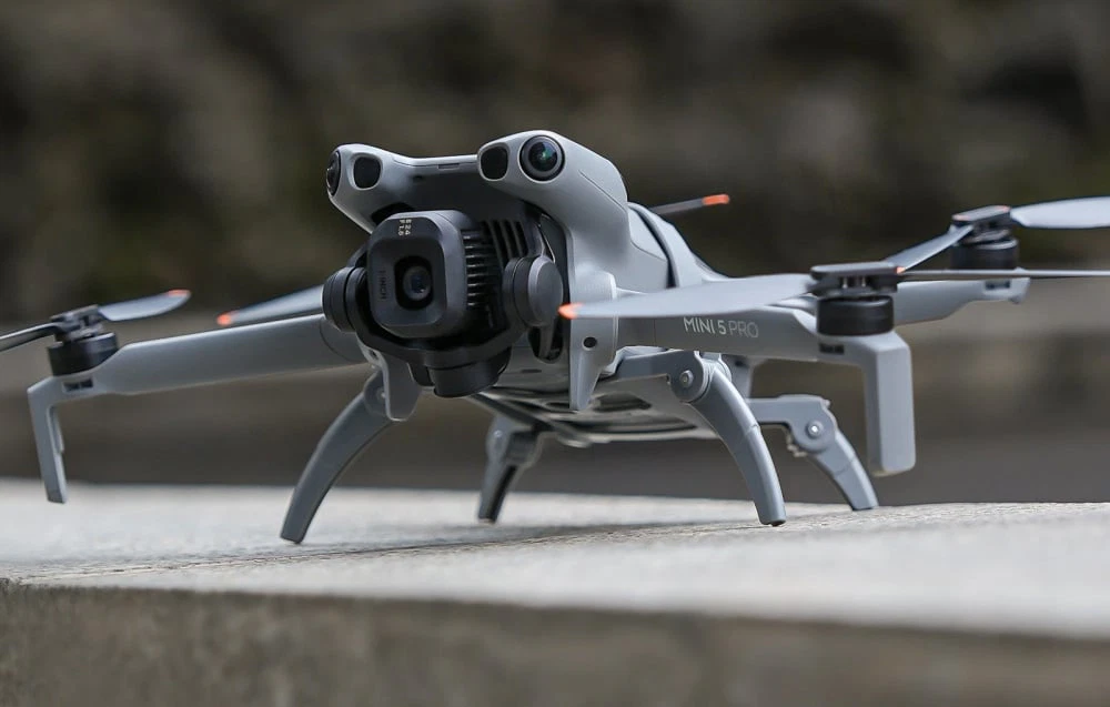 Dronă DJI Mini 5 Pro în picioare pe o suprafață de beton, cu picioarele întinse pentru aterizare