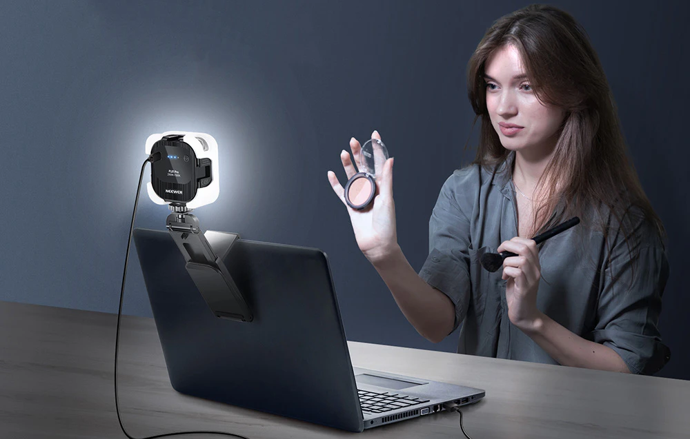 O femeie în fața unui laptop care se machiază, iluminată de o lampă LED montată în spate