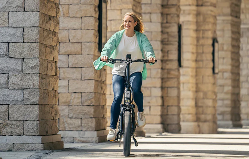 O femeie merge pe o bicicletă electrică între coloane de piatră