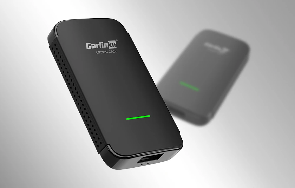 Adaptorul negru CarlinKit CPC200-CP2A cu un LED verde, prezentat pe un fundal deschis, cu un al doilea dispozitiv estompat în fundal