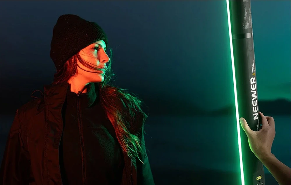 O femeie cu o pălărie închisă la culoare, iluminată din lateral de lumina verde și roșie a unei lămpi alungite.