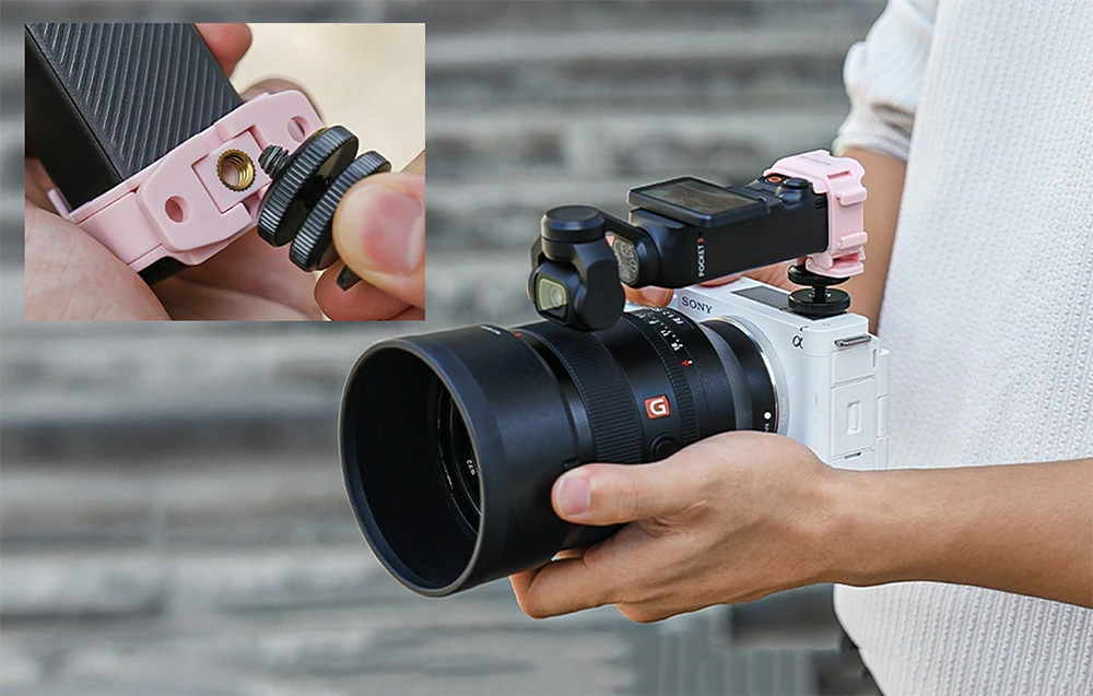 O persoană ține în mână o cameră Sony cu un obiectiv mare pe care este montată o cameră mică DJI Pocket în suportul de montare roz
