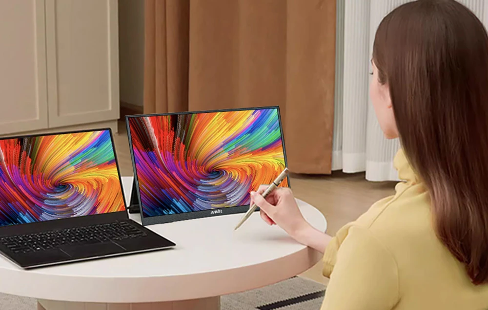 O femeie folosește un stylus pe ecranul unui monitor portabil așezat lângă un laptop.