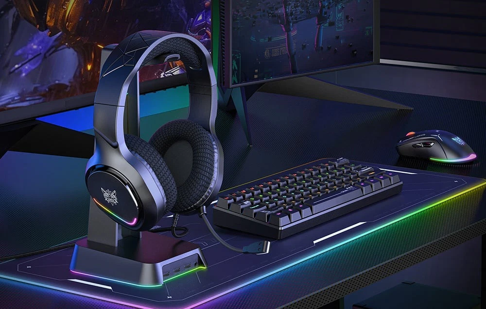 Căști așezate pe suport lângă tastatură și mouse de gaming pe un suport retroiluminat RGB de pe birou