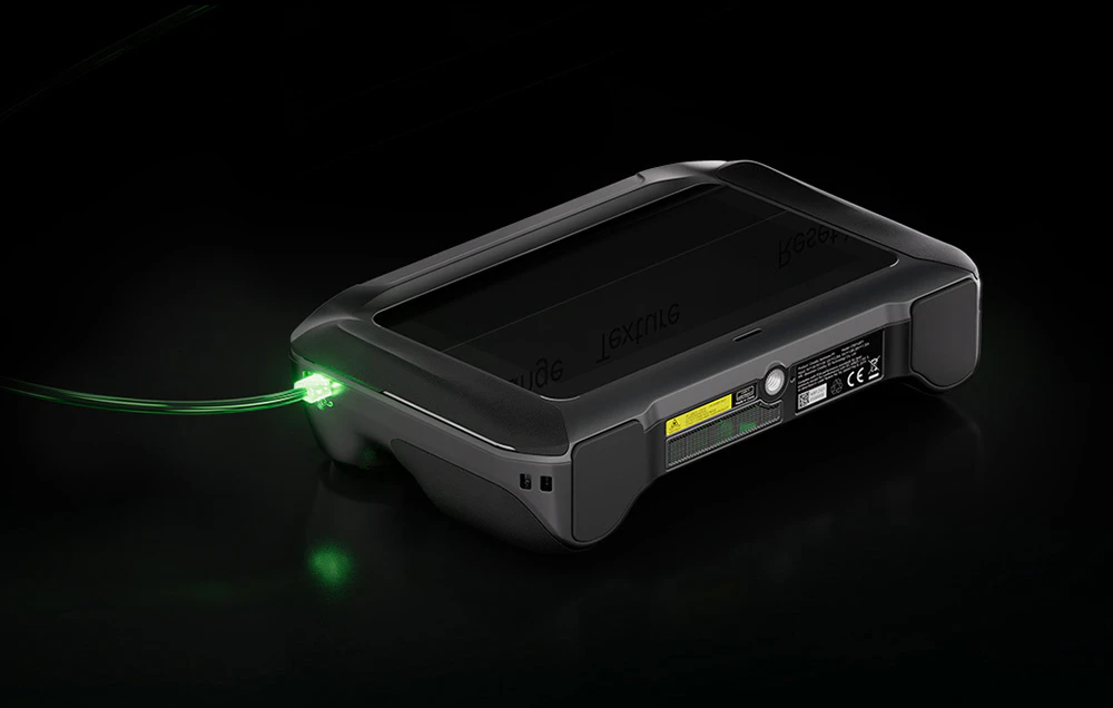 Un scaner 3D Creality așezat pe o suprafață neagră și conectat la un încărcător cu un cablu verde luminos