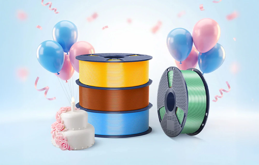 Trei bobine de material colorat așezate lângă un tort și baloane pe un fundal albastru deschis.