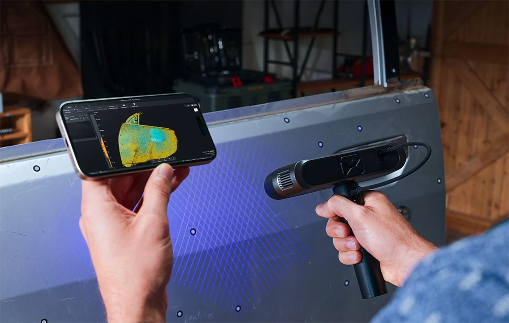 O persoană folosește un scaner 3D portabil pentru a scana o componentă metalică în timp ce vizualizează modelul pe ecranul unui smartphone