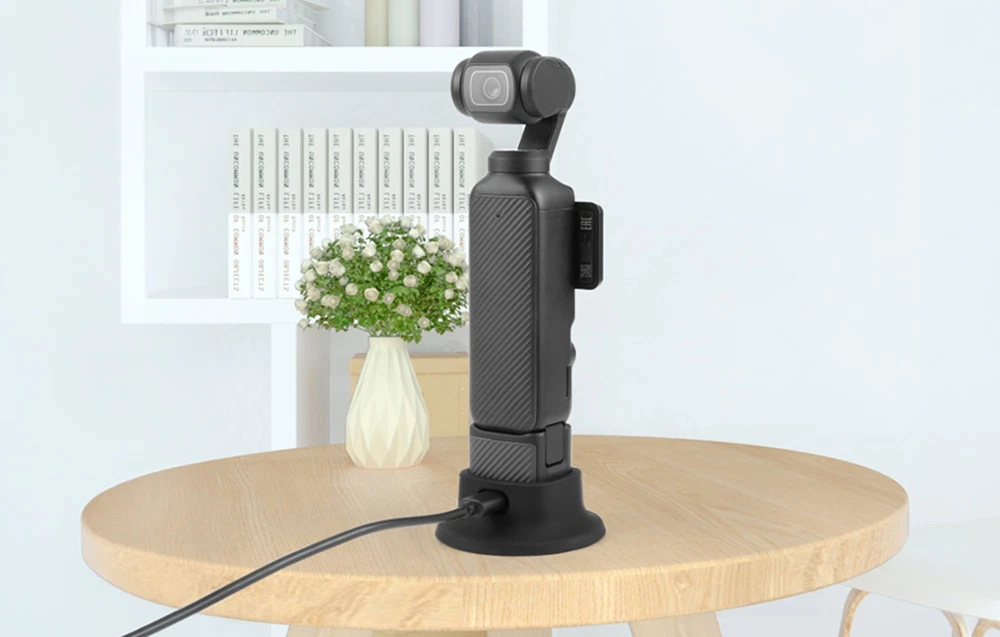 Camera DJI Osmo Pocket 3 montată într-un suport din silicon negru pe o masă de lemn într-o cameră luminoasă.