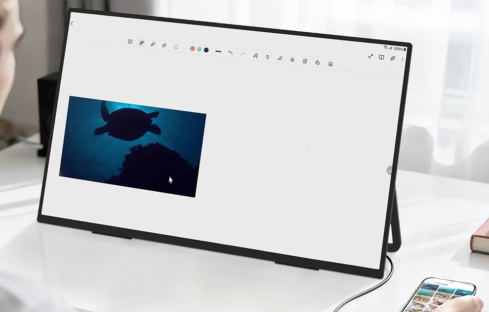 Monitor portabil conectat la un smartphone, afișând o aplicație de luat notițe și editare foto pe un birou