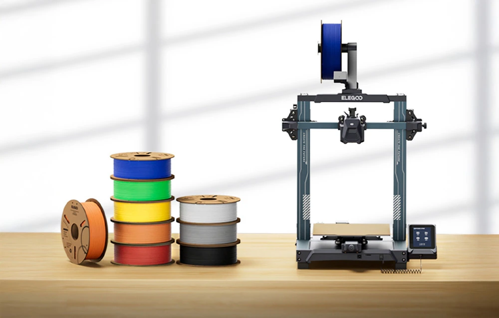 Imprimantă 3D ELEGOO pe o masă din lemn lângă bobine colorate de filament