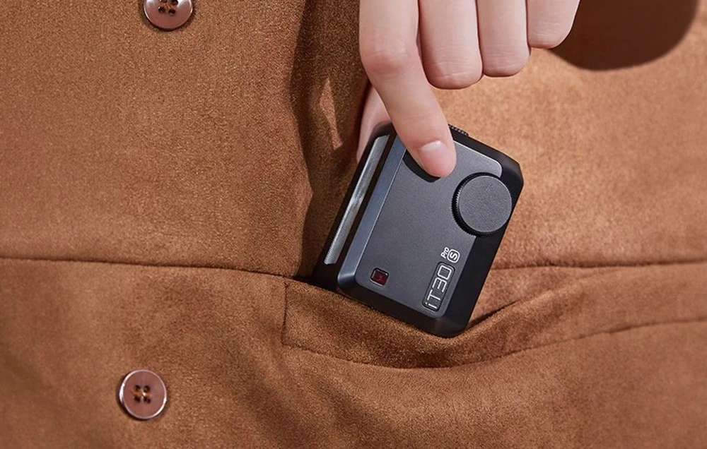 O mână care introduce mini-blitzul Godox iT30 Pro negru într-un buzunar mic al unei jachete din piele de căprioară