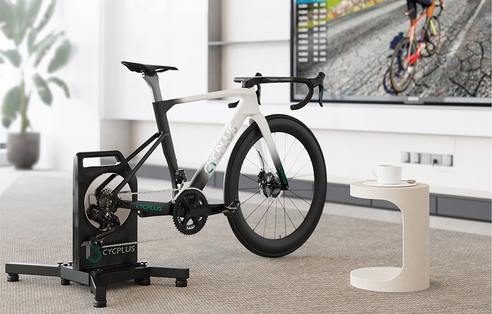 Bicicletă albă de șosea pe trainerul Cycplus T3 în camera de zi cu ecran TV
