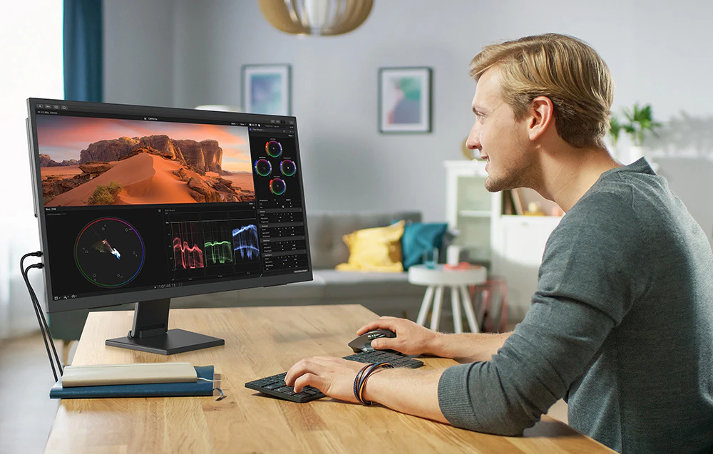 Bărbat la un birou editând videoclipuri sau grafică pe un monitor cu diagrame și imagini.