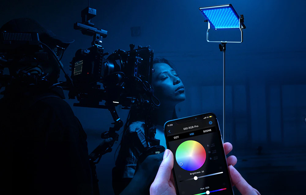 Un platou de filmare cu o femeie iluminată cu lumină LED albastră, un cameraman cu o cameră și un telefon cu o aplicație pentru a controla luminile de la distanță