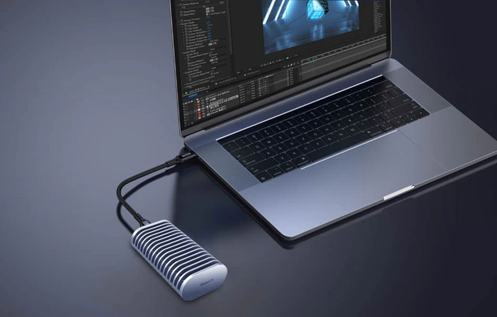 O carcasă compactă pentru SSD TerraMaster conectată printr-un cablu la un laptop așezat pe un birou întunecat.