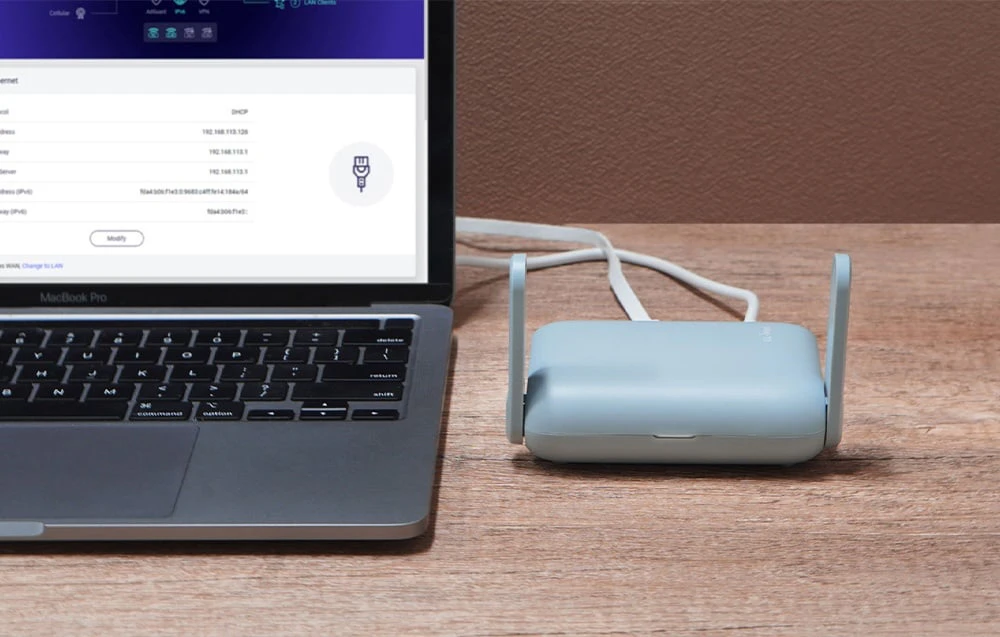 Routerul se află pe o măsuță maro lângă un laptop