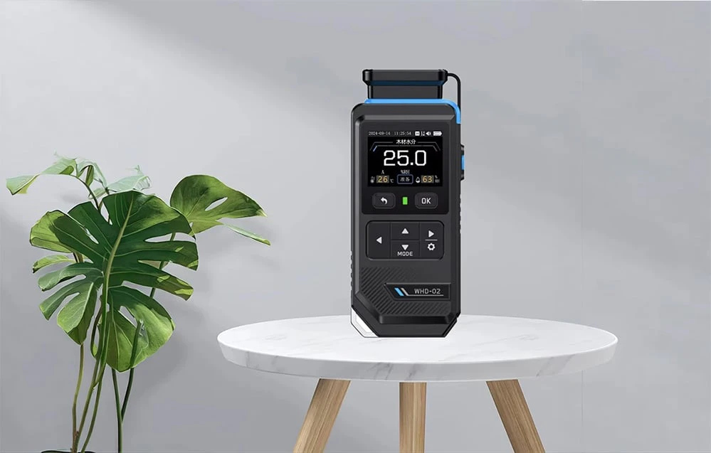 Higrometru electronic WHD-02 așezat pe o masă albă lângă o plantă în ghiveci