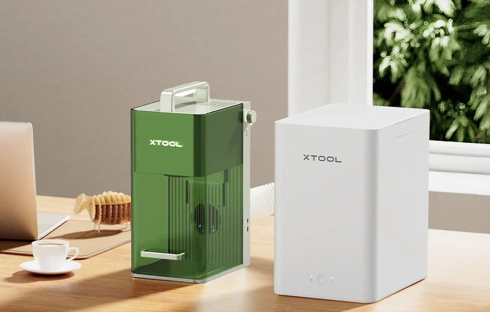 Un tăietor cu laser verde conectat printr-un furtun flexibil de evacuare la un aspirator de fum xTool alb.