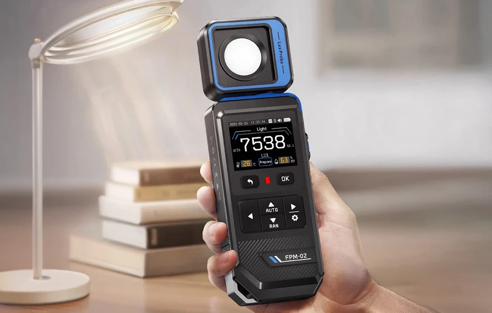 Un bărbat ține în mână un luxmetru digital, măsurând lumina unei lămpi de birou aflată lângă o stivă de cărți